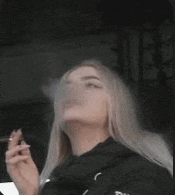 a woman is smoking a cigarette in a car while wearing a black jacket .