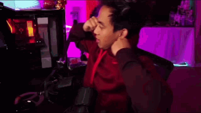 a person in a red shirt is sitting in front of a microphone in a dark room .