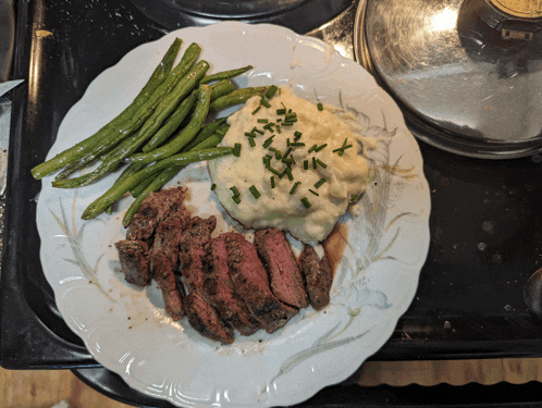 a plate of steak green beans and mashed potatoes on a stove top