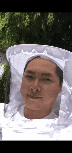 a man wearing a beekeeper hat looks at the camera with trees in the background