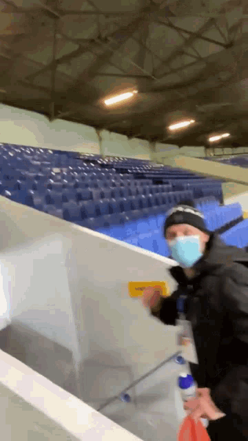 a man wearing a mask stands in a stadium with blue seats