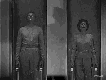 a black and white photo of a man and woman standing next to each other in a glass case .