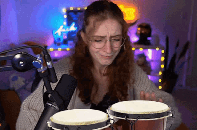 a woman playing bongo drums in front of a microphone with a neon sign that says fender in the background