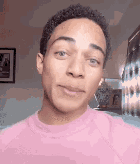 a young man wearing a pink sweater is looking at the camera .