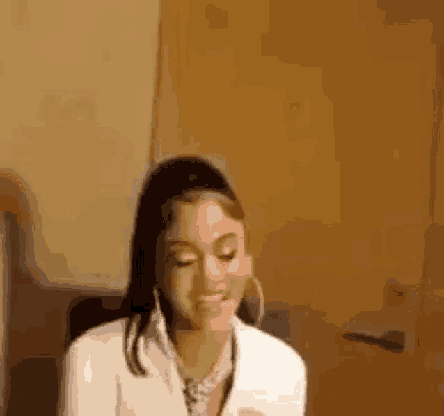 a woman wearing hoop earrings and a white shirt is sitting in front of a door and smiling .