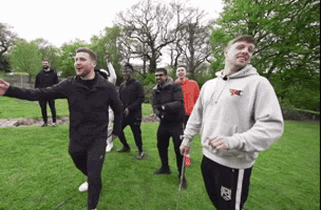 a group of men are standing in a grassy field and one of them is wearing a hoodie that says fc on it .