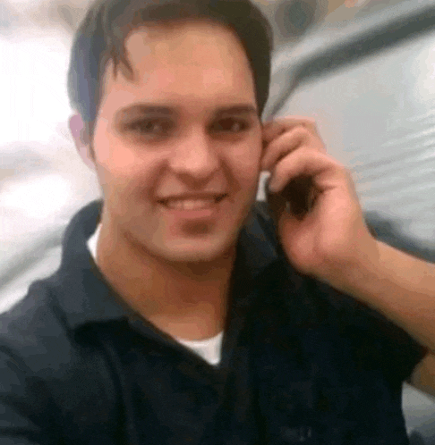 a man in a black shirt is smiling while talking on a cell phone .