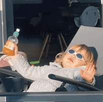 a little girl wearing sunglasses is sitting in a chair holding a bottle