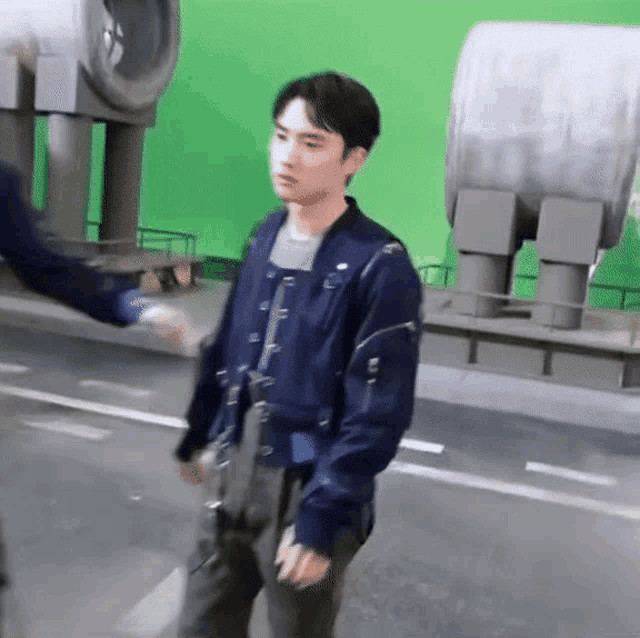 a man in a blue jacket is walking down a street with a green screen in the background .