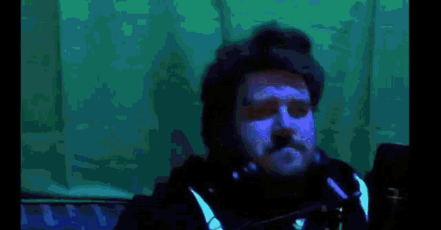 a man with a beard is wearing headphones in front of a green curtain