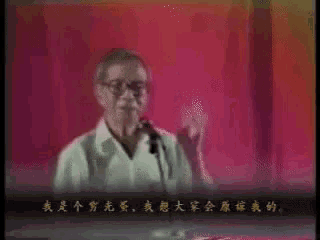 a man speaking into a microphone in front of a red curtain with chinese writing on it