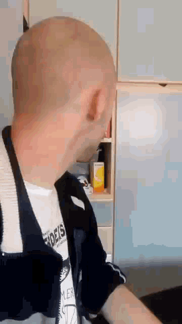 a bald man wearing a t-shirt that says ' eoeis ' on it is standing in a kitchen