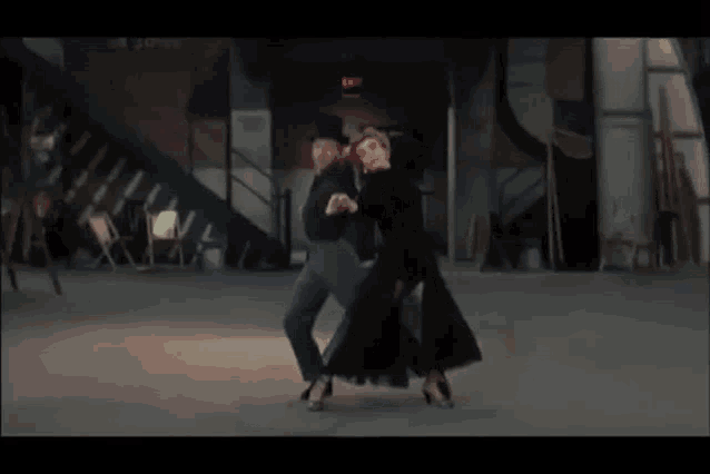 a man is kneeling on the ground while a woman stands behind him in front of an exit sign