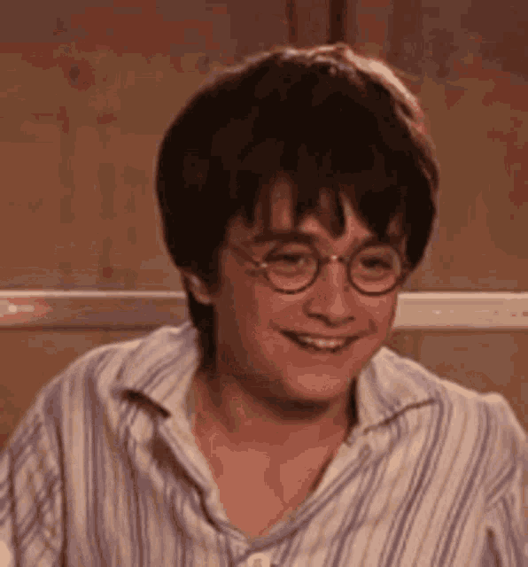 harry potter wearing glasses and a striped shirt is smiling .