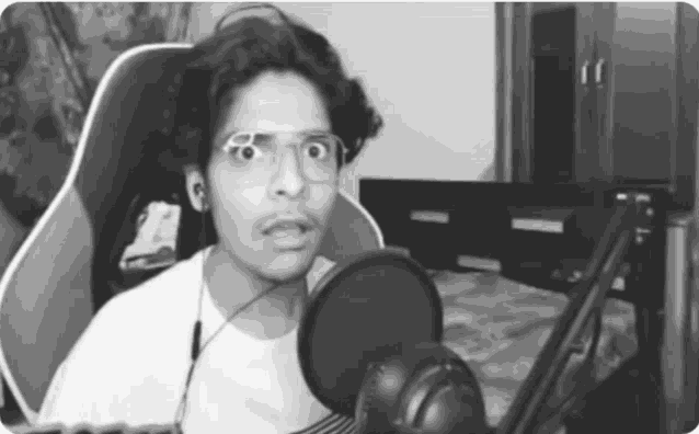 a black and white photo of a man wearing glasses and headphones in front of a microphone .
