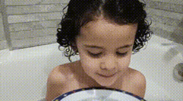 a little girl is sitting in a bathtub holding a bowl .