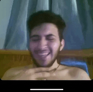 a shirtless man with a beard is smiling while sitting in front of a window .