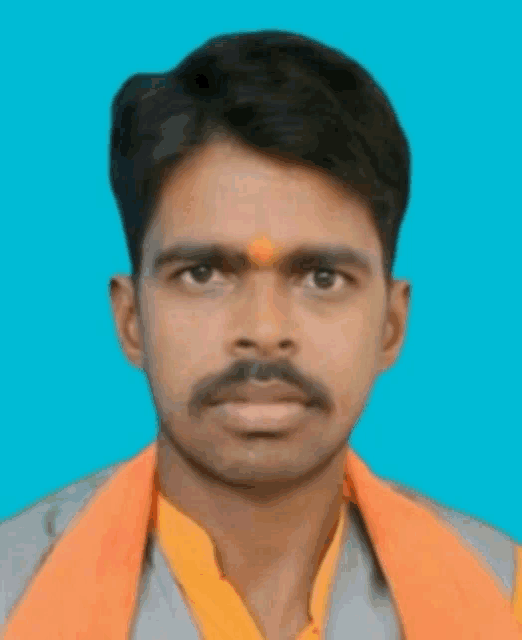 a man with an orange scarf around his neck looks at the camera with a blue background