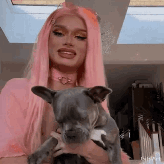 a woman with pink hair is holding a small dog in her arms