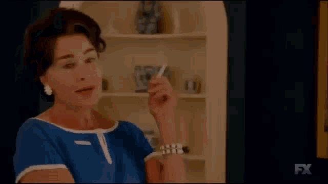 a woman in a blue dress is smoking a cigarette in front of a fx logo