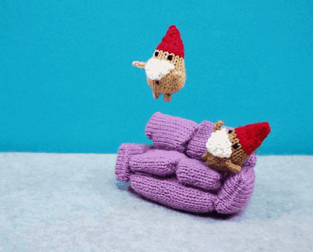 a purple knitted couch with two knitted gnomes on it