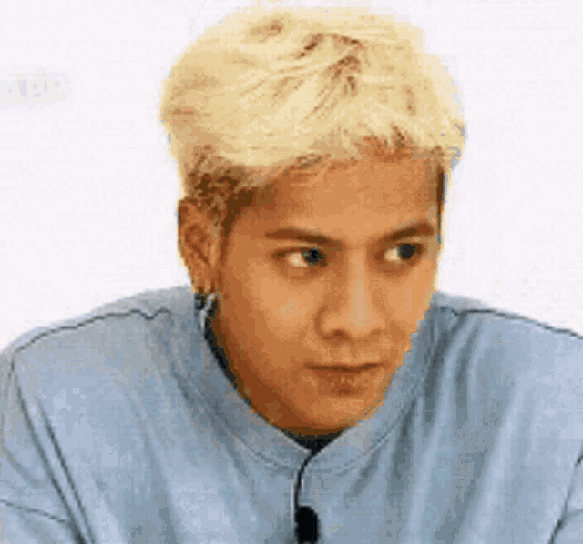 a man with blonde hair and earrings is wearing a blue shirt and making a funny face .
