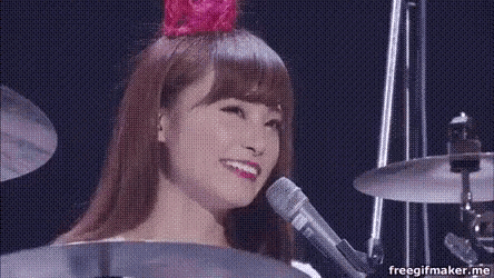 a woman is playing drums and singing into a microphone while wearing a pink flower in her hair .