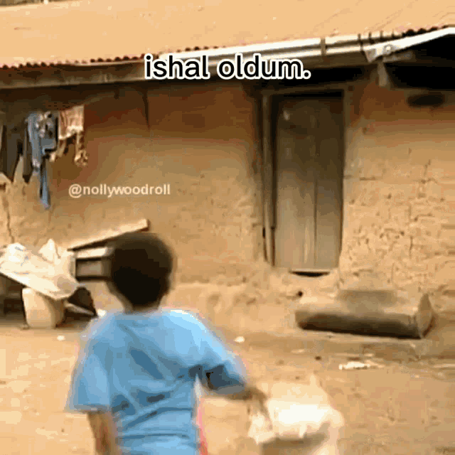 a boy in a blue shirt is standing in front of a building with the words ishal oldum above him