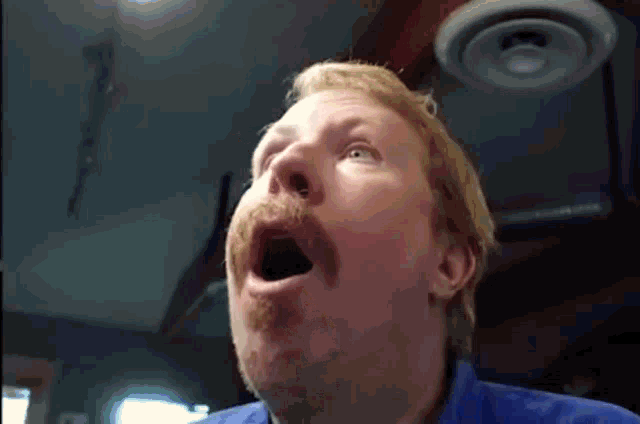 a man with a beard and mustache is yawning with his mouth open .