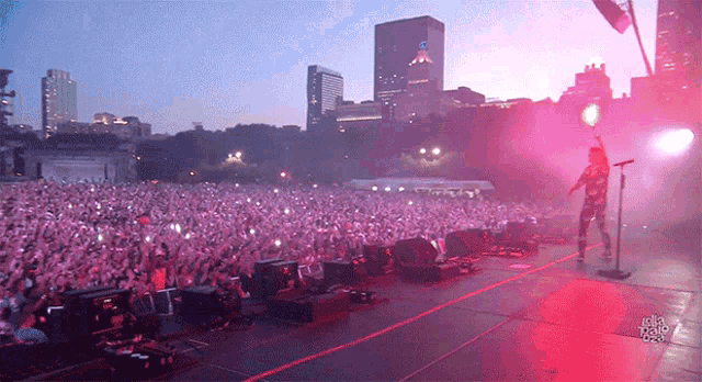 a man singing into a microphone in front of a crowd at a concert with a city in the background