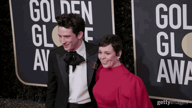 a man in a tuxedo and a woman in a red dress pose on a red carpet in front of a golden globe sign