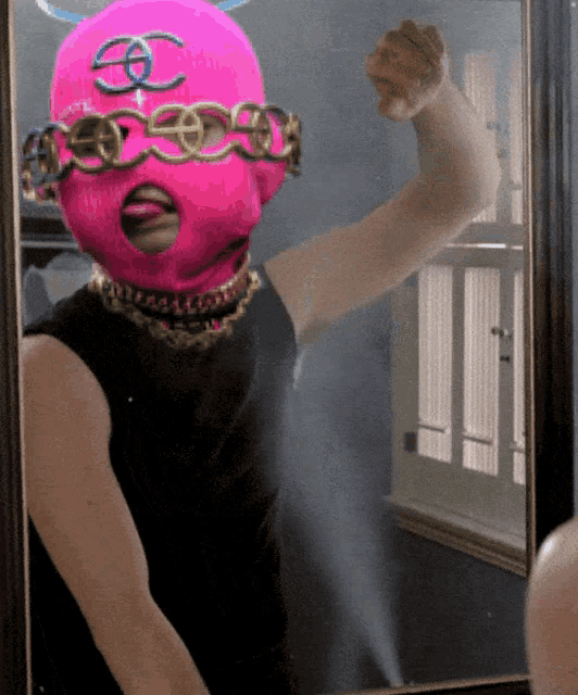 a woman wearing a pink mask with a chanel logo on it stands in front of a mirror