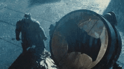 batman and robin are fighting each other in the rain while batman is standing next to a barrel .