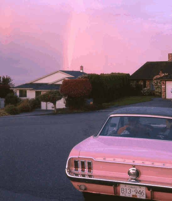 a pink mustang is parked in front of a house with a rainbow in the background