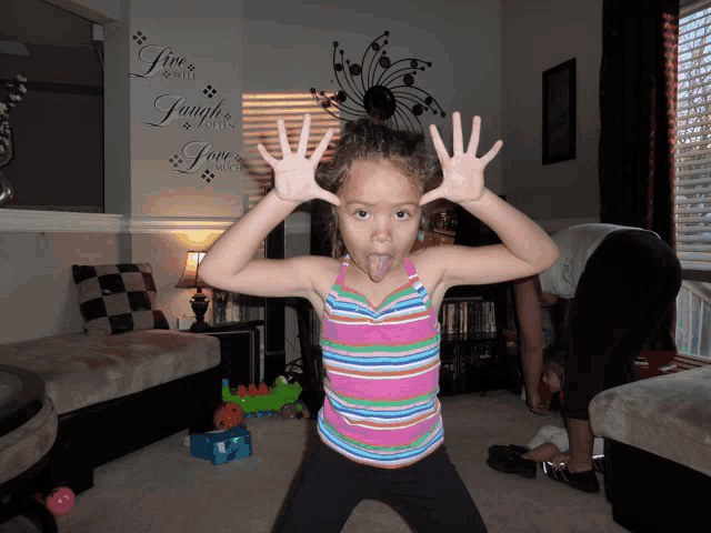 a little girl making a funny face in front of a wall decal that says live laugh love