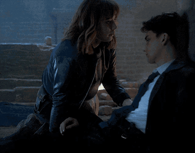 a woman in a leather jacket sits on a man 's lap in a dark room