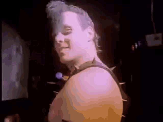 a man with a mohawk is standing in a dark room with spikes on his back .