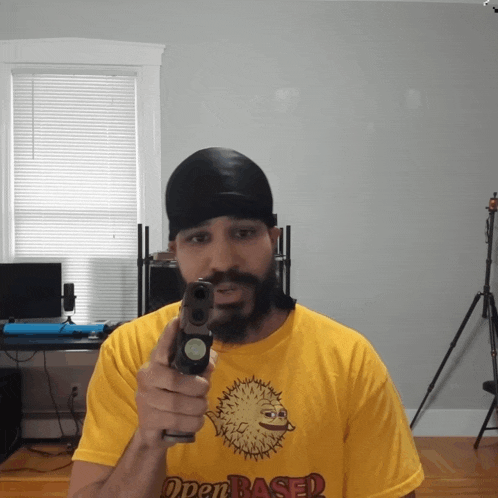 a man with a beard wearing a yellow open based shirt holds a gun