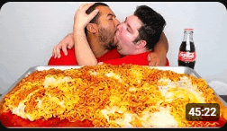 two men are kissing in front of a pan of spaghetti and a coca cola bottle .