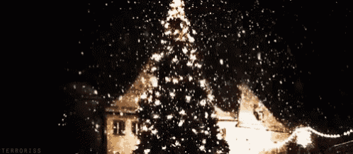 a christmas tree is lit up at night and snow is falling around it .