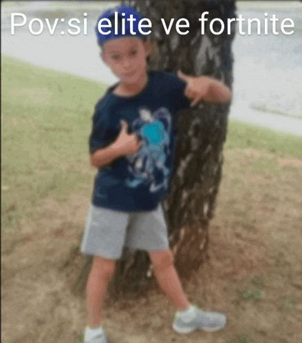 a young boy is standing next to a tree and giving a thumbs up sign