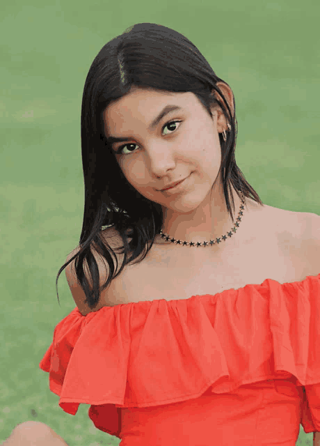 a girl wearing a red off the shoulder top and a necklace with stars on it