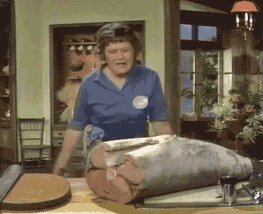 a woman in a blue shirt is standing in front of a large piece of meat on a table .