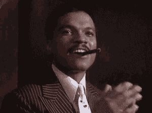 a man in a suit and tie is clapping his hands and smoking a cigar .