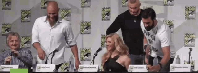 a group of people are sitting at a table with a comic con sign behind them