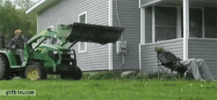 a man is sitting in a chair in front of a house while a tractor is moving a bucket .