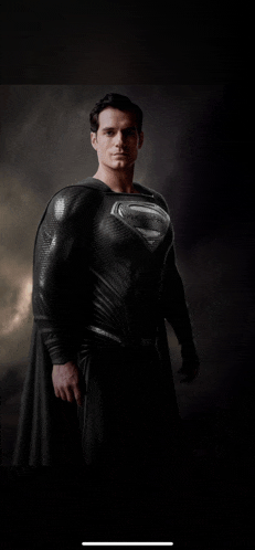 a man in a black superman costume stands in a dark room