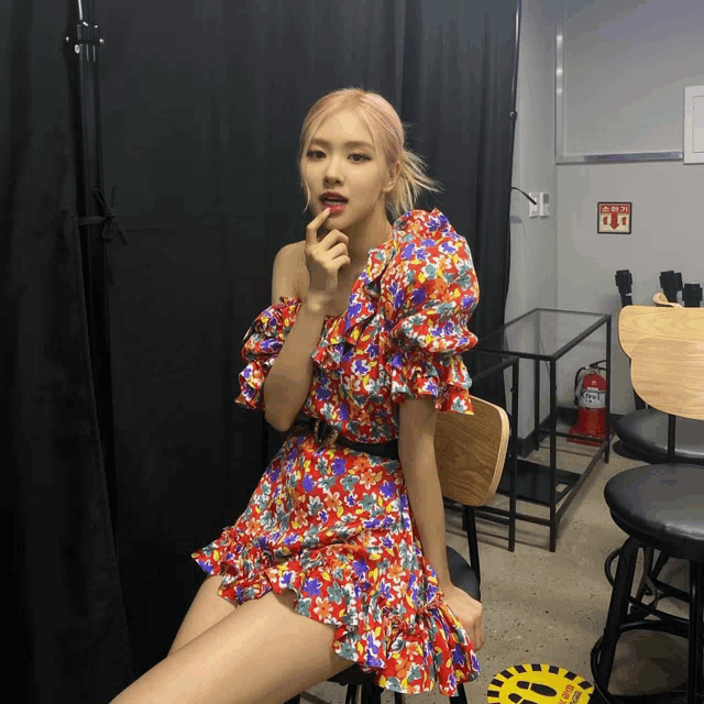 a woman in a floral dress is sitting on a chair in front of a fire extinguisher