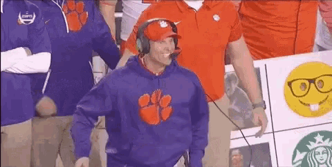 a man wearing a purple hoodie with a clemson logo on it stands in front of a starbucks sign .