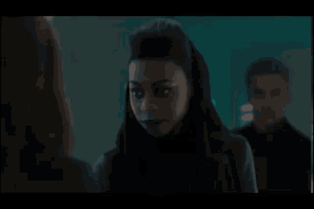 a woman in a suit stands in front of a man in a black shirt